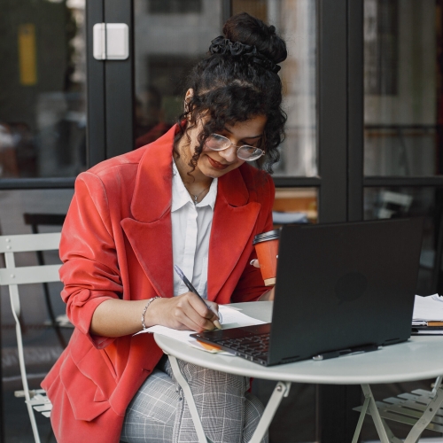 Indian woman working on a laptop in a street cafe. Wearing stylish smart clothes -  jacket, glasses